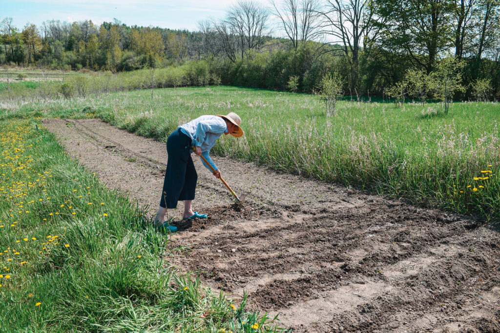A woman wearing a straw hat tills a garden