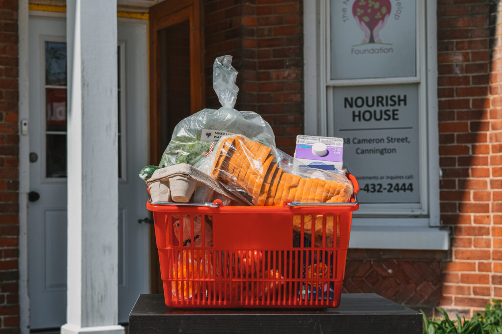 A red basket of groceries in front of Nourish House Food Bank