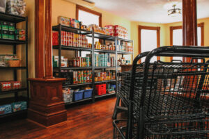 Foreground: shopping carts Background: stocked shelves with groceries inside Nourish House Food Bank