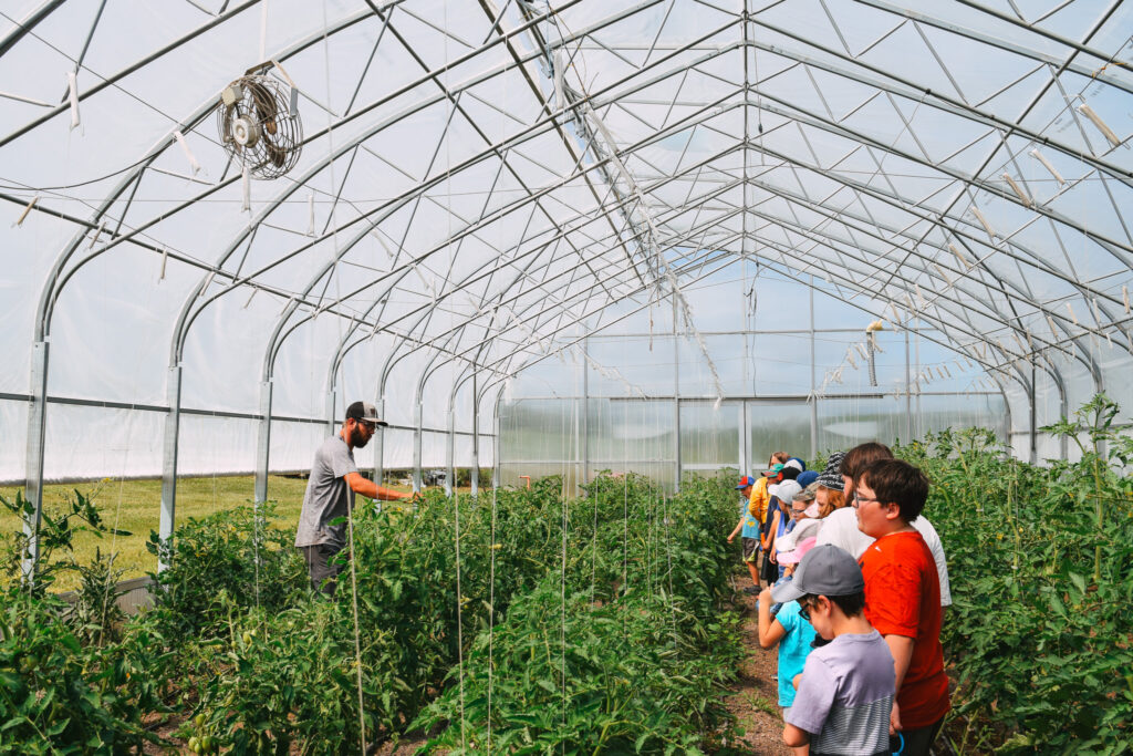 Children observe a farmer in a greenhouse during one of our summer camps.