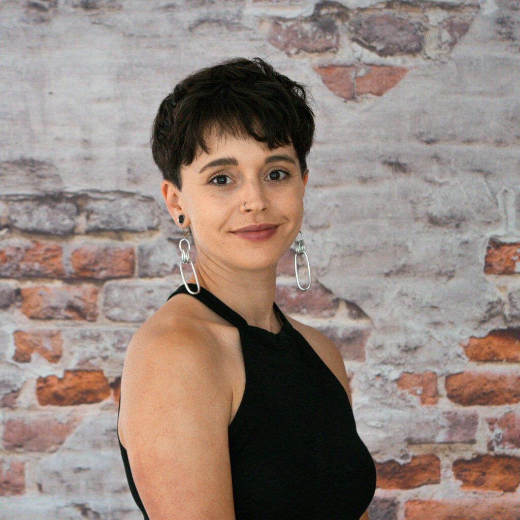 Headshot of Zoe, our People and Culture Manager, in front of a brick wall.