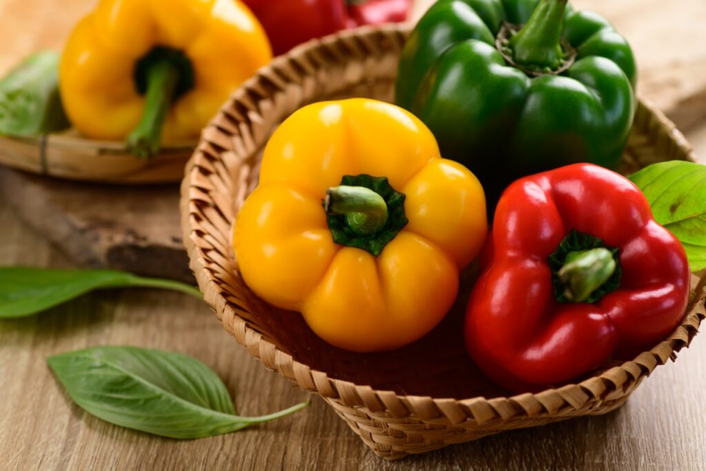 Fresh yellow, red and green bell peppers in a bamboo basket on wooden background, Organic vegetables