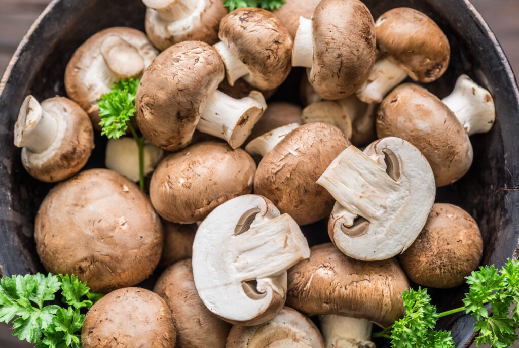 Brown colored edible mushrooms or cremini mushrooms on wooden table with herbs. Top view.