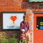 A man and his 4 year old daughter stand in front of the TNDF logo