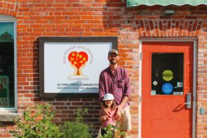 A man and his 4 year old daughter stand in front of the TNDF logo