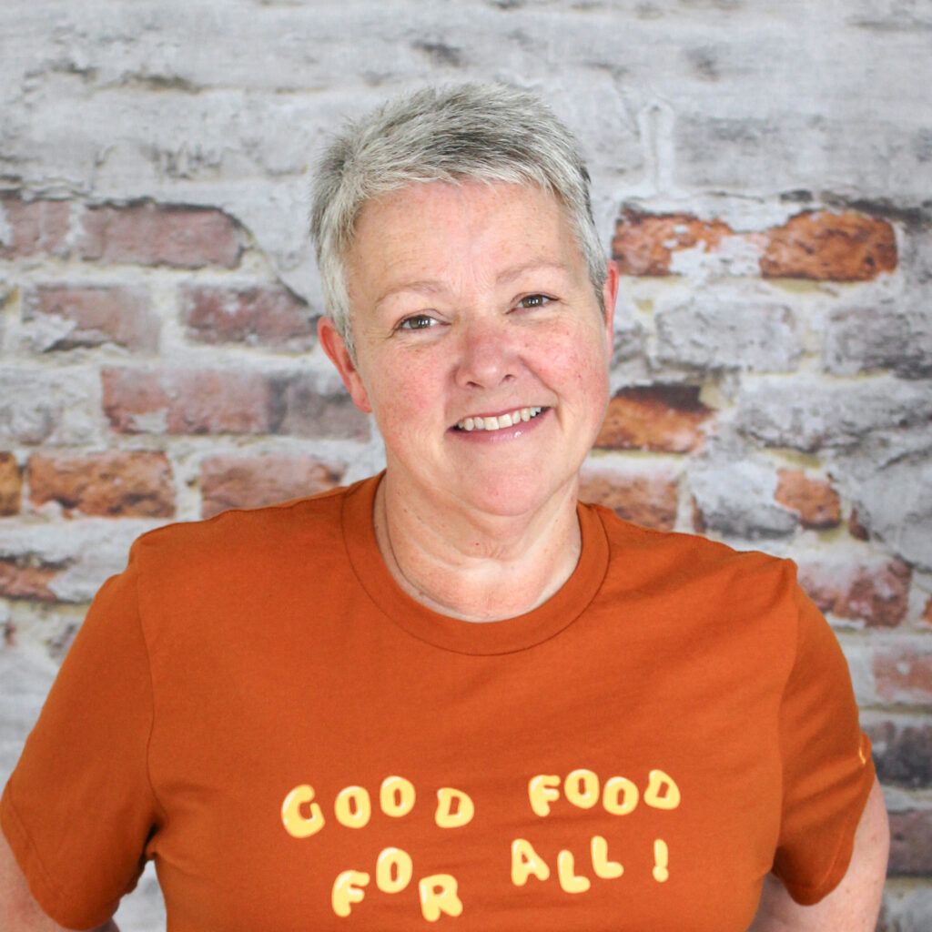 Headshot of Jenn, our Receptionist & Volunteer Coordinator, in front of a brick wall.