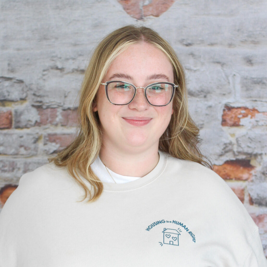 Headshot of Jess, our Executive Director, in front of a brick wall.