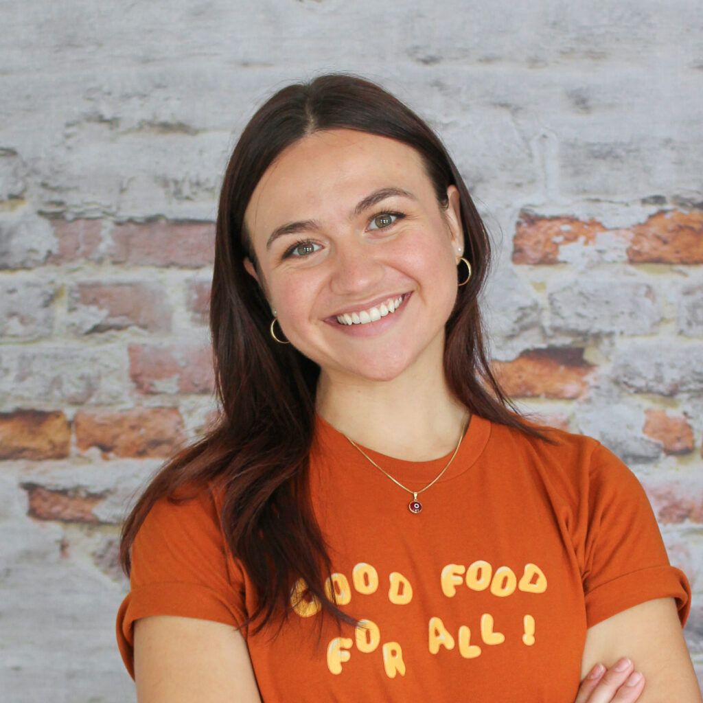 Headshot of Katerina, our Fundraising and Advocacy Coordinator, in front of a brick wall.