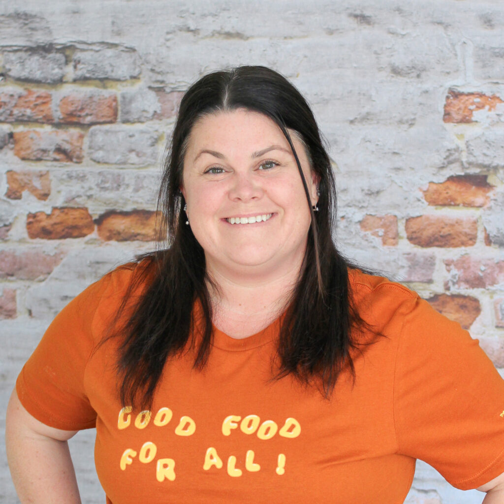 Headshot of Kori in front of a brick wall.