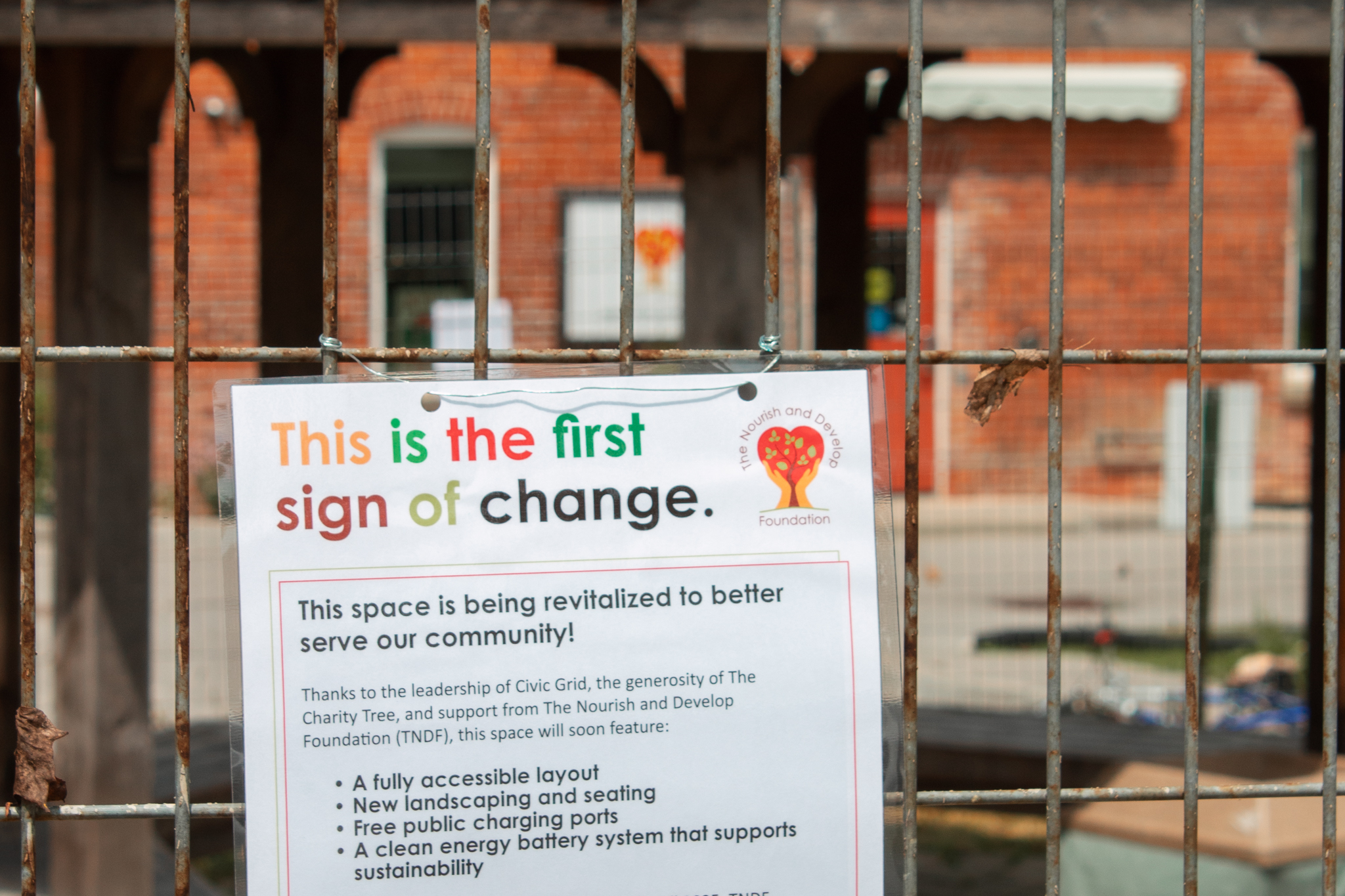 A sign hanging from a chain link fence reading "This is the first sign of change"