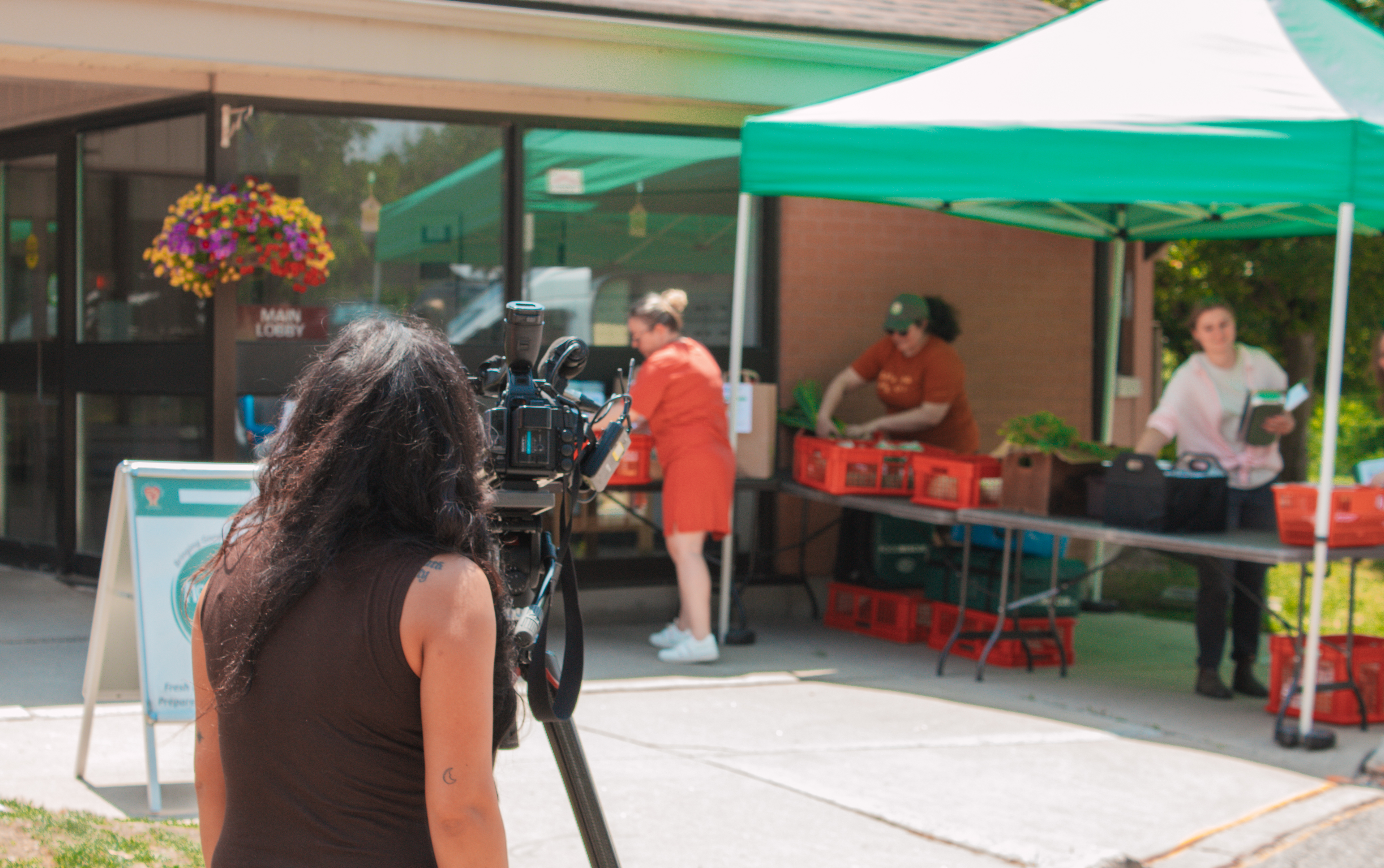 A global news reporter standing in front of a tripod directs the camera to Mobile Food Market
